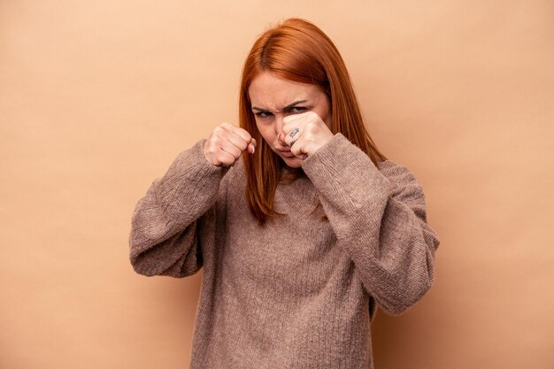 Photo young caucasian woman isolated on beige background throwing a punch anger fighting due to an argument boxing