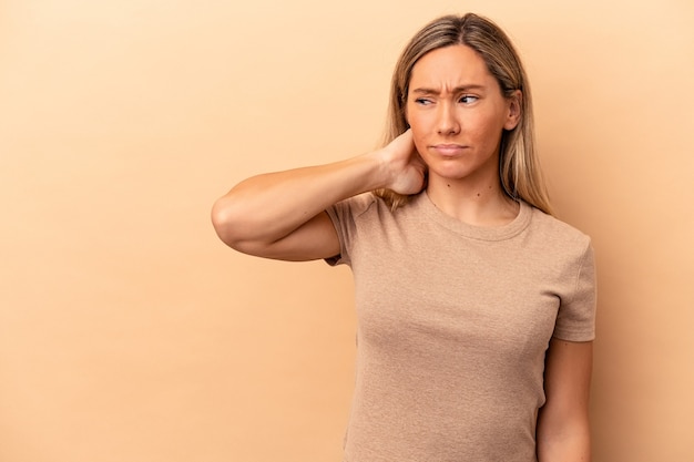 Young caucasian woman isolated on beige background touching back of head, thinking and making a choice.