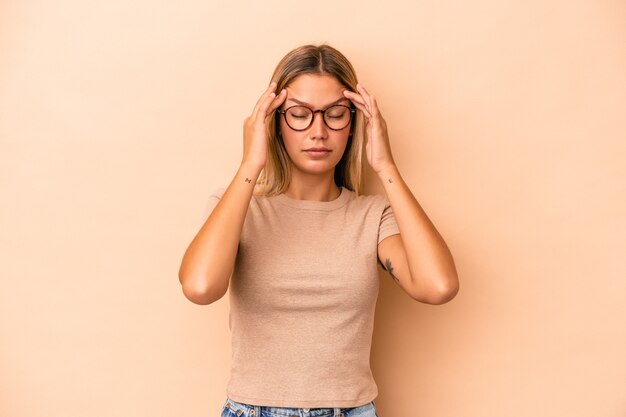 寺院に触れて頭痛を持っているベージュの背景に分離された若い白人女性。