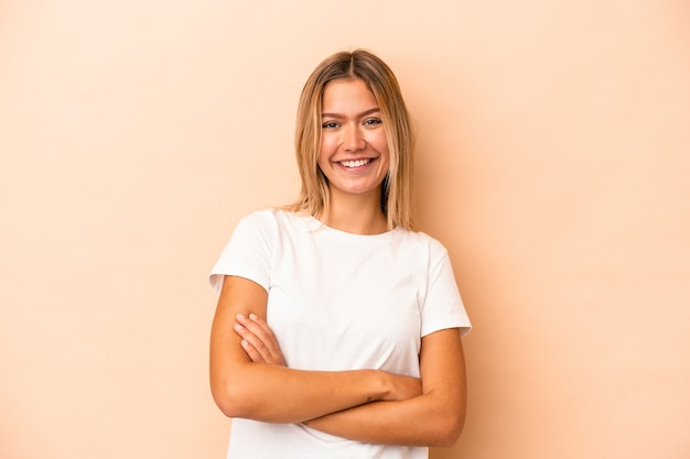 Young caucasian woman isolated on beige background who feels confident, crossing arms with determination.