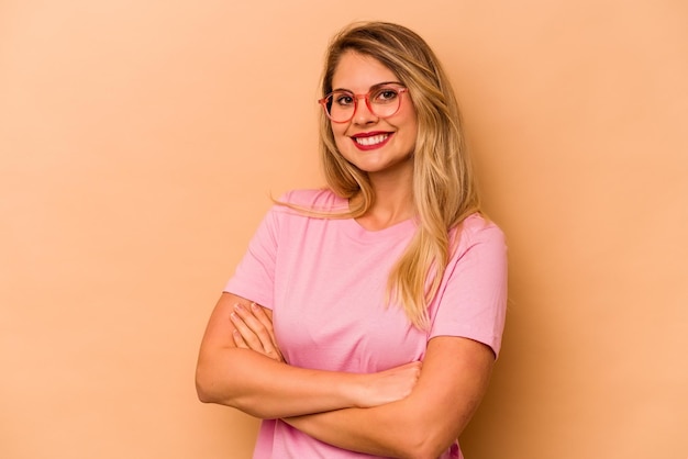 Young caucasian woman isolated on beige background who feels confident crossing arms with determination