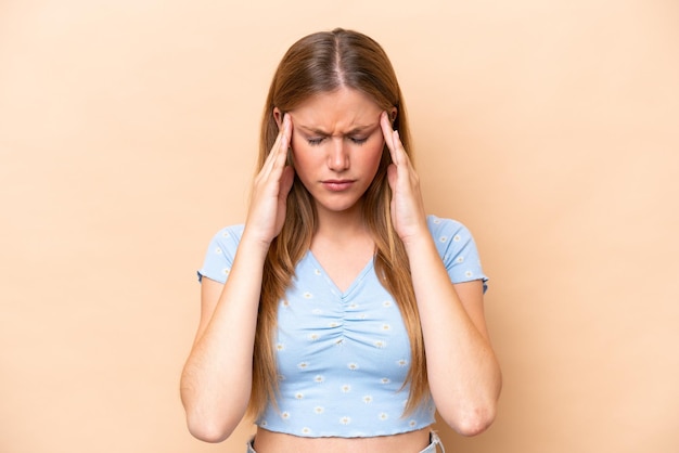 Young caucasian woman isolated on beige background with headache