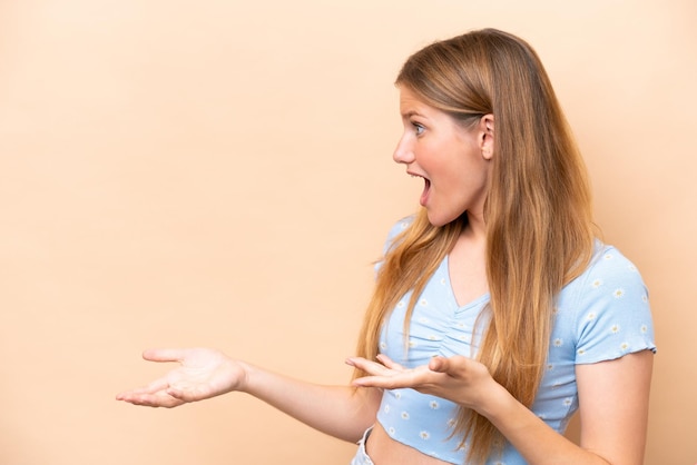 Young caucasian woman isolated on beige background with surprise expression while looking side