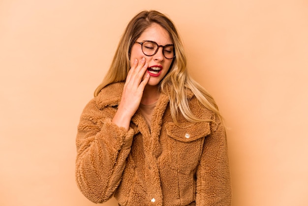 Young caucasian woman isolated on beige background yawning showing a tired gesture covering mouth with hand