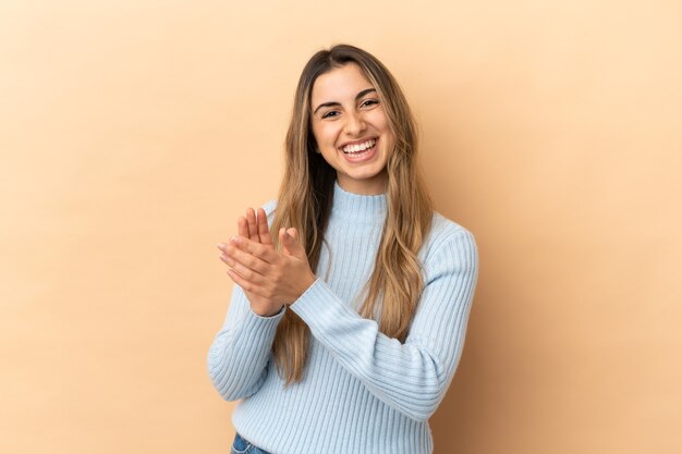 Young caucasian woman isolated on beige wall applauding after presentation in a conference