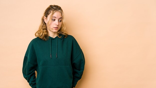 Young caucasian woman isolated on beige wall being shocked because of something she has seen