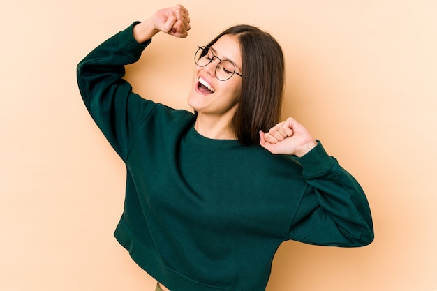 Young caucasian woman isolated on beige wall celebrating a special day, jumps and raise arms with energy.