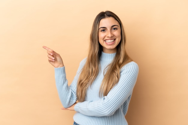 Young caucasian woman isolated on beige wall happy and pointing up