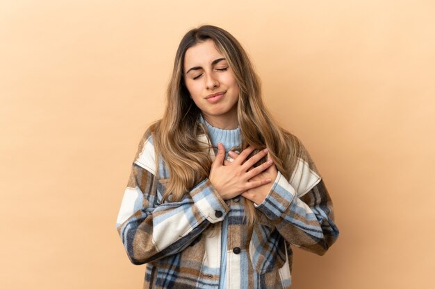 Young caucasian woman isolated on beige wall having a pain in the heart