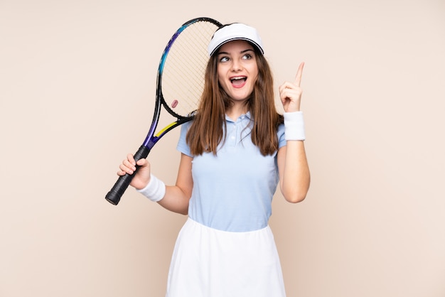 Young caucasian woman isolated on beige wall playing tennis and pointing up