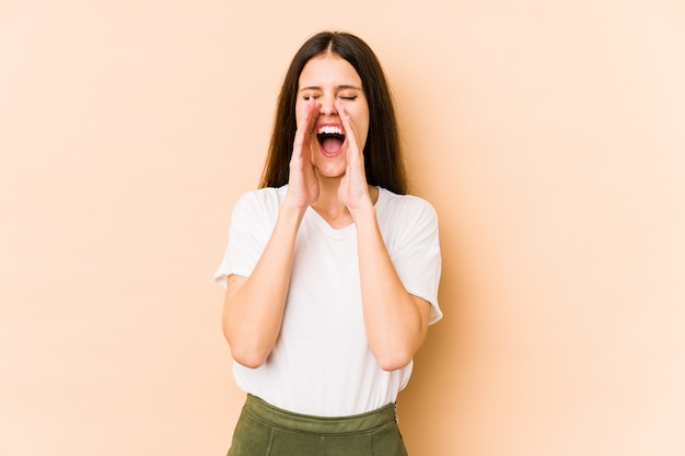 Young caucasian woman isolated on beige wall shouting excited to front.