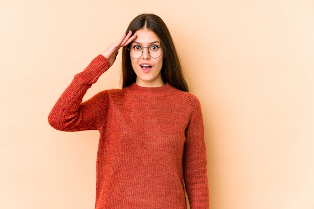 Young caucasian woman isolated on beige wall shouts loud, keeps eyes opened and hands tense.