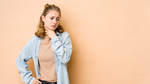 Young caucasian woman isolated on beige wall suffers pain in throat due a virus or infection.