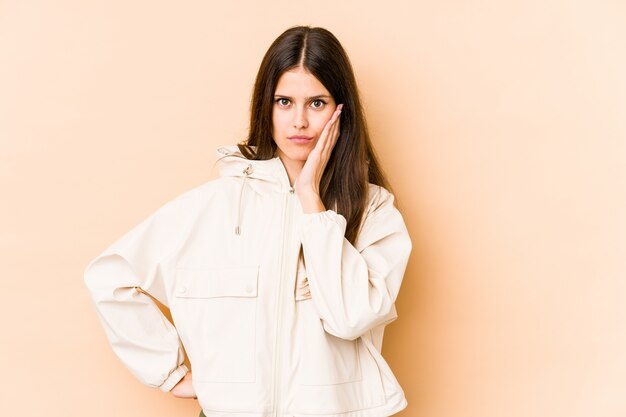 Young caucasian woman isolated on beige wall who feels sad and pensive, looking at copy space.