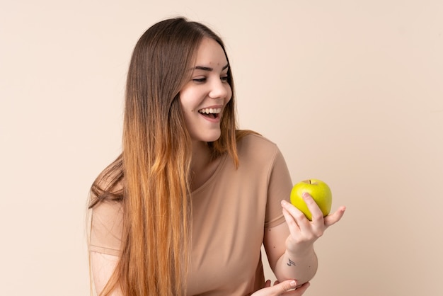 Молодая кавказская женщина изолированная на бежевой стене с яблоком и счастливая