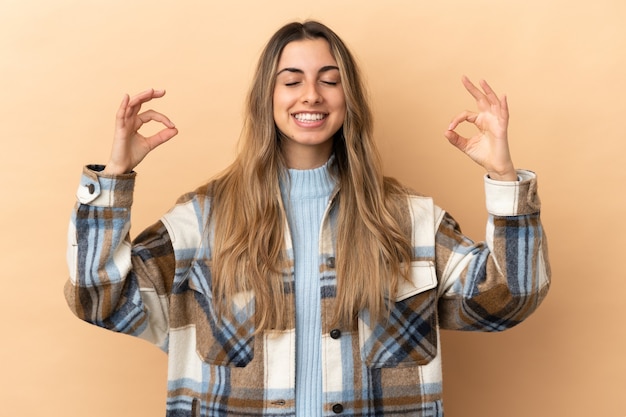 Young caucasian woman isolated on beige wall in zen pose