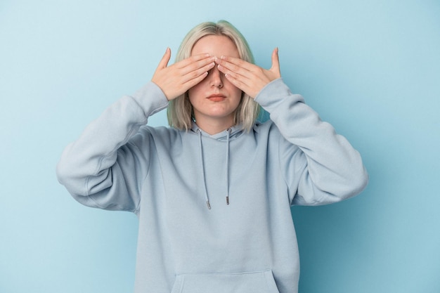 Young caucasian woman isolated on blue background afraid covering eyes with hands.