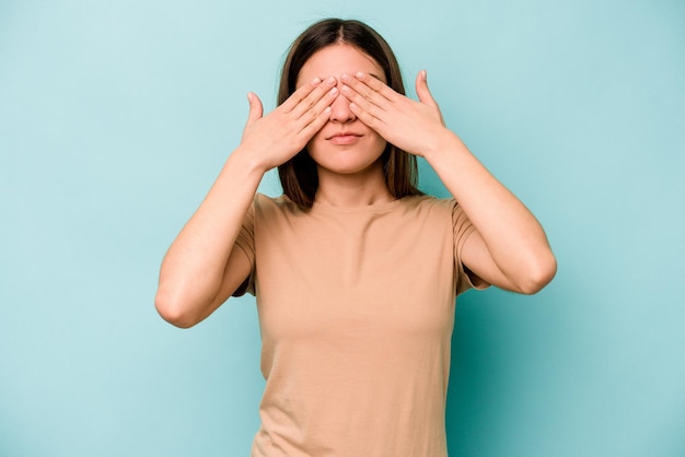 Young caucasian woman isolated on blue background afraid covering eyes with hands