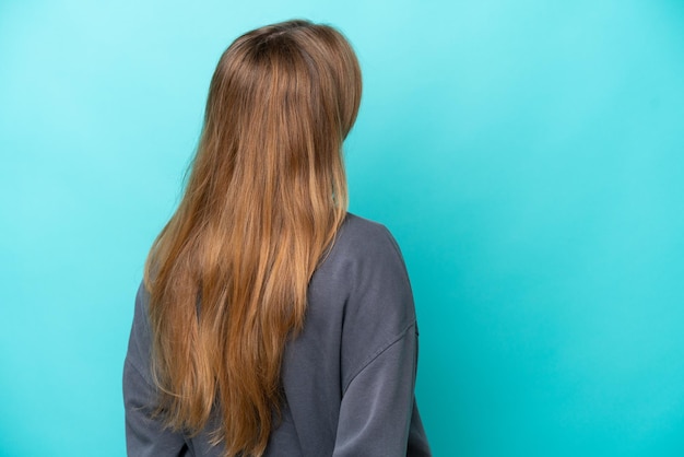 Young caucasian woman isolated on blue background in back position and looking back