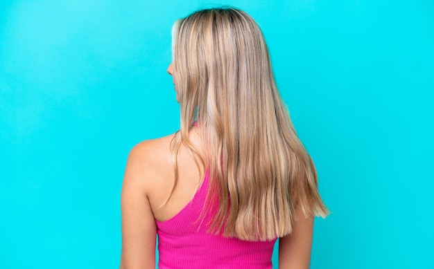 Young caucasian woman isolated on blue background in back position and looking side