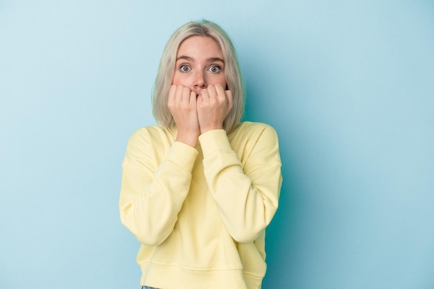 Young caucasian woman isolated on blue background biting fingernails, nervous and very anxious.