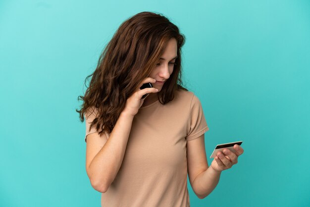 Young caucasian woman isolated on blue background buying with the mobile with a credit card