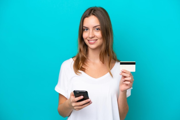 Young caucasian woman isolated on blue background buying with the mobile with a credit card