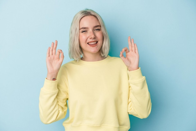 Young caucasian woman isolated on blue background cheerful and confident showing ok gesture.