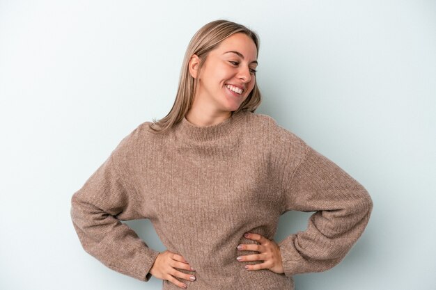 Photo young caucasian woman isolated on blue background confident keeping hands on hips.