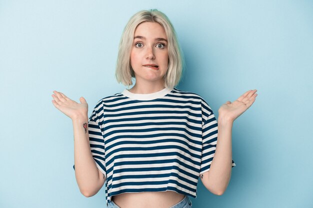 Young caucasian woman isolated on blue background confused and doubtful shrugging shoulders to hold a copy space.