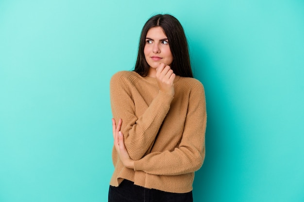 Young caucasian woman isolated on blue background confused, feels doubtful and unsure.