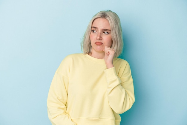 Young caucasian woman isolated on blue background confused, feels doubtful and unsure.