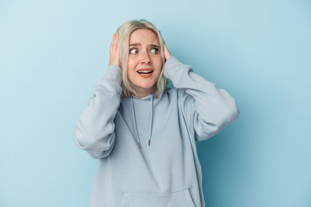 Young caucasian woman isolated on blue background covering ears with hands trying not to hear too loud sound.