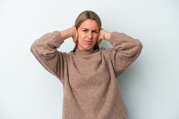 Young caucasian woman isolated on blue background covering ears with hands.