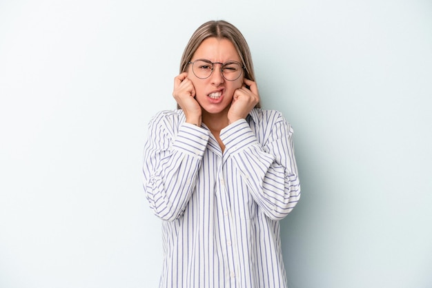 Young caucasian woman isolated on blue background covering ears with hands.