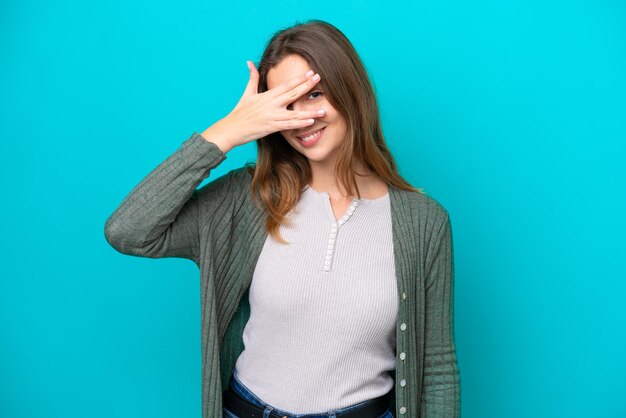 Young caucasian woman isolated on blue background covering eyes by hands and smiling