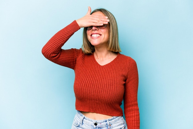 Young caucasian woman isolated on blue background covers eyes with hands smiles broadly waiting for a surprise