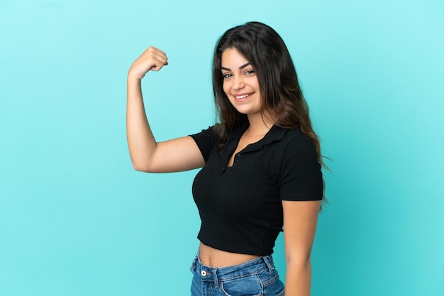 Young caucasian woman isolated on blue background doing strong gesture