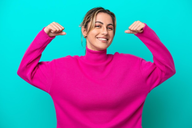 Young caucasian woman isolated on blue background doing strong gesture