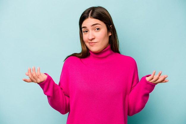 Photo young caucasian woman isolated on blue background doubting and shrugging shoulders in questioning gesture