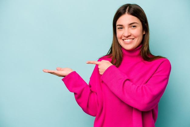 Young caucasian woman isolated on blue background excited holding a copy space on palm