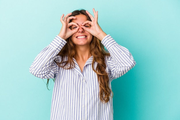 Young caucasian woman isolated on blue background  excited keeping ok gesture on eye.
