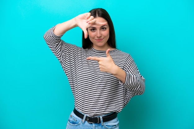 Young caucasian woman isolated on blue background focusing face\
framing symbol