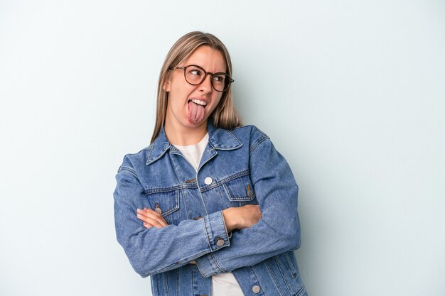 Young caucasian woman isolated on blue background funny and friendly sticking out tongue.