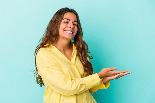 手のひらにコピースペースを保持している青い背景で隔離の若い白人女性。