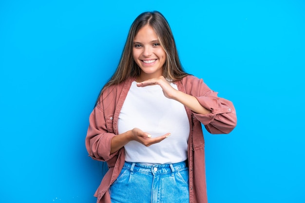 Giovane donna caucasica isolata su sfondo blu che tiene copyspace immaginario sul palmo per inserire un annuncio