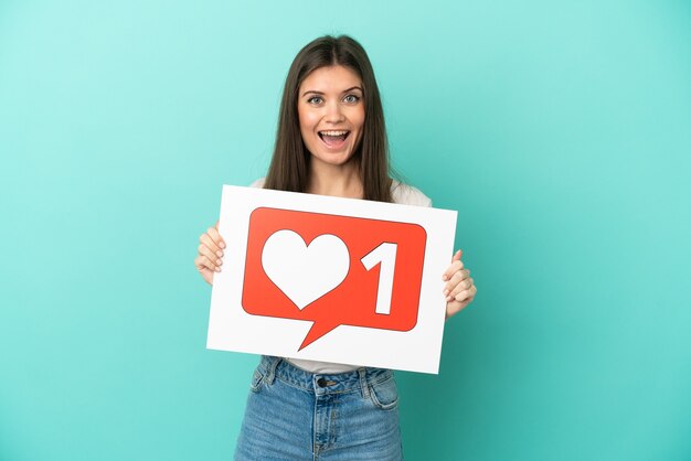 Photo young caucasian woman isolated on blue background holding a placard with like icon with happy expression