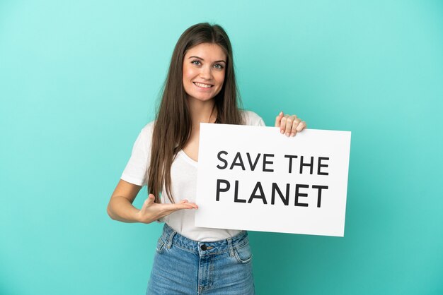 Young caucasian woman isolated on blue background holding a placard with text Save the Planet and pointing it