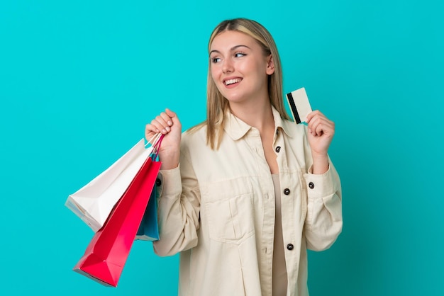 Young caucasian woman isolated on blue background holding shopping bags and a credit card