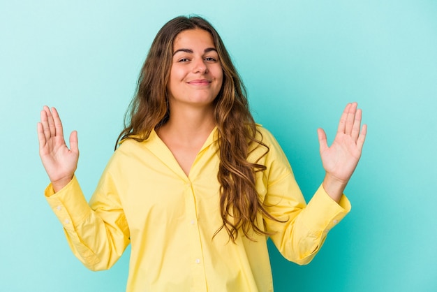 Young caucasian woman isolated on blue background  holding something little with forefingers, smiling and confident.